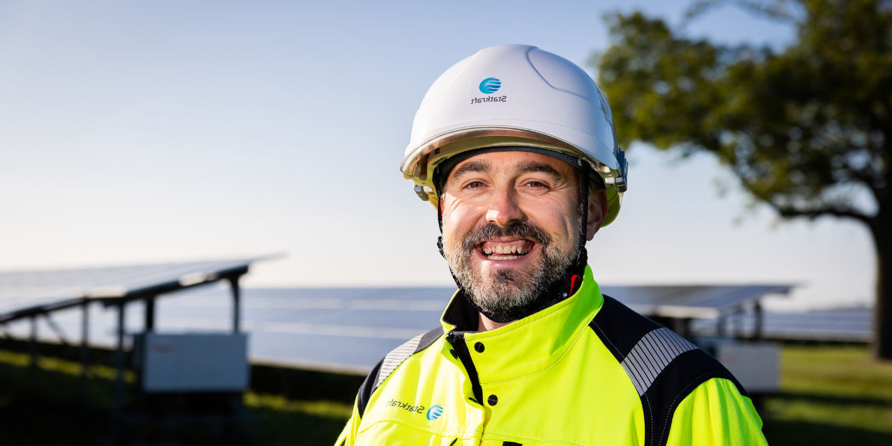 Man wearing safety gear smiling with solar panels in the background